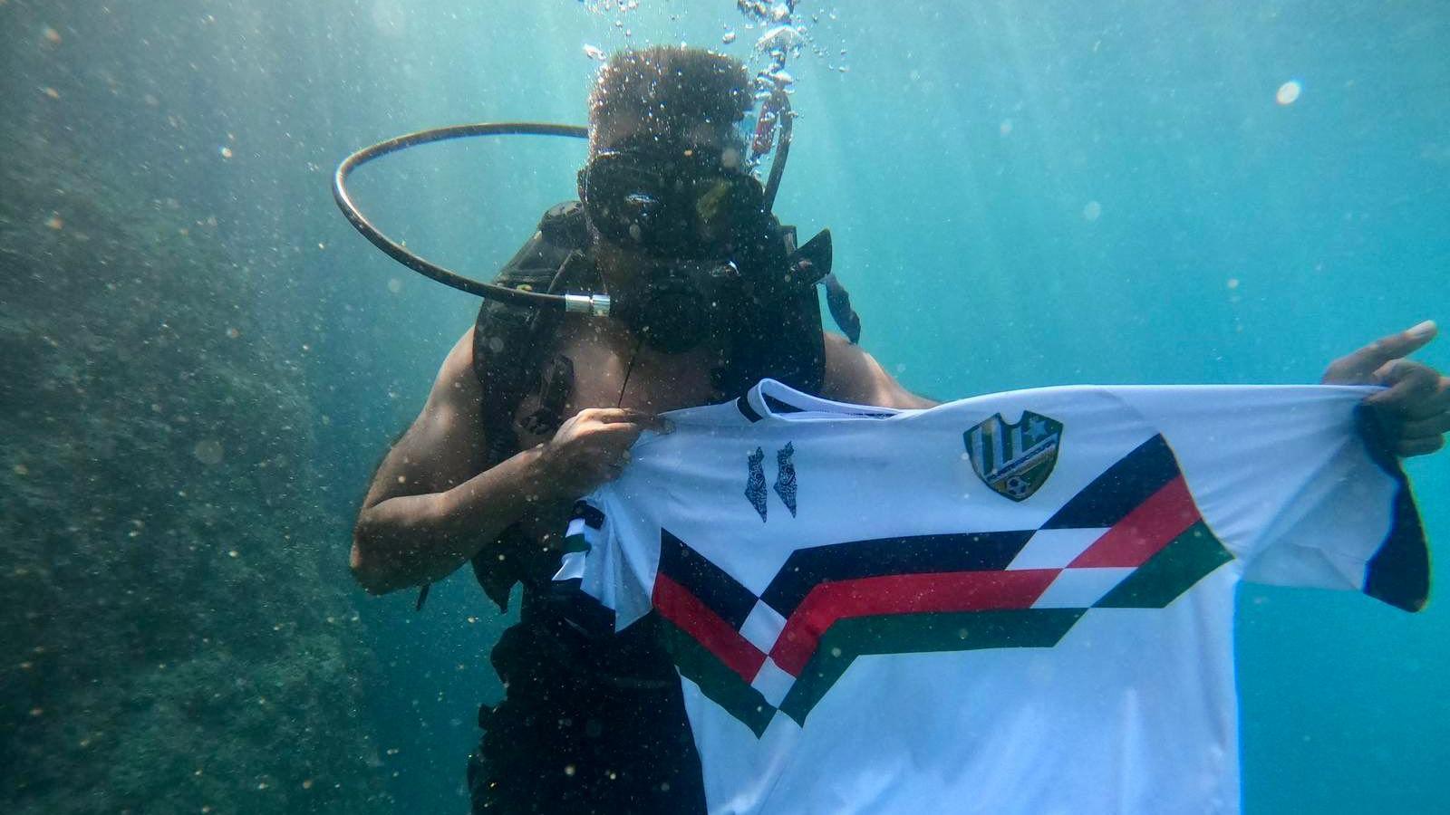 Arif Aziz in the Mediterranean Sea on a scuba dive. He is holding up his FC Peterborough football shirt under the water