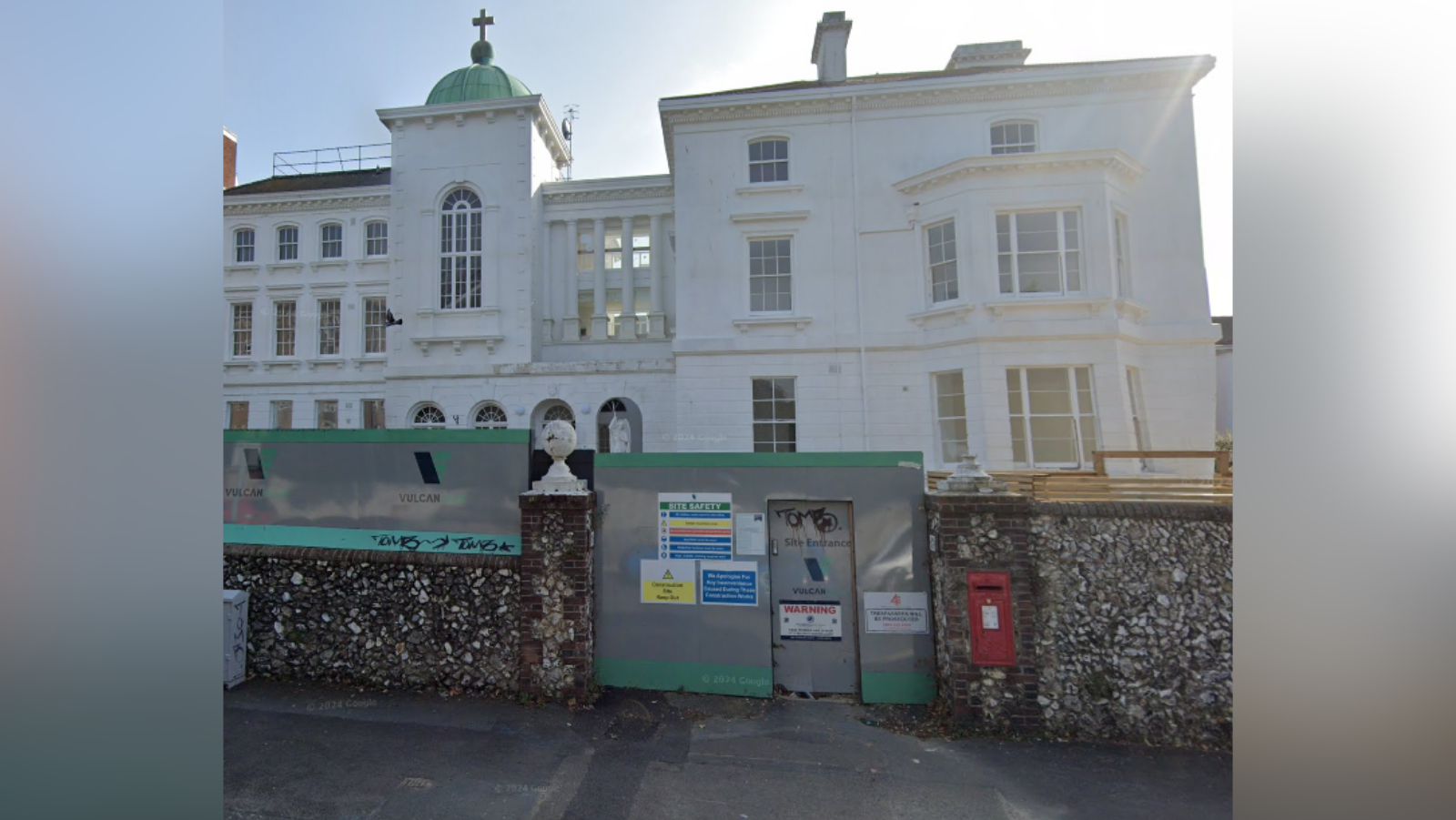 The former Esperance Hospital in Eastbourne which closed in 2019. The white building is inaccessible from the gate and has been boarded up with signage. There is a green circular structure and cross on the roof. 