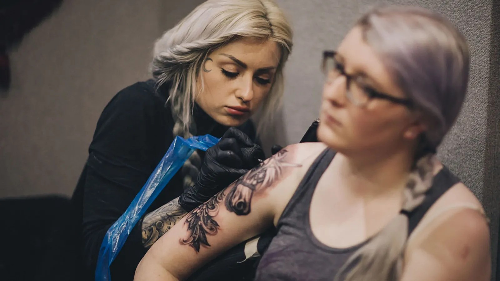 A woman tattoos antoerh woman on her arm. Credit Mykola Romanovksy.