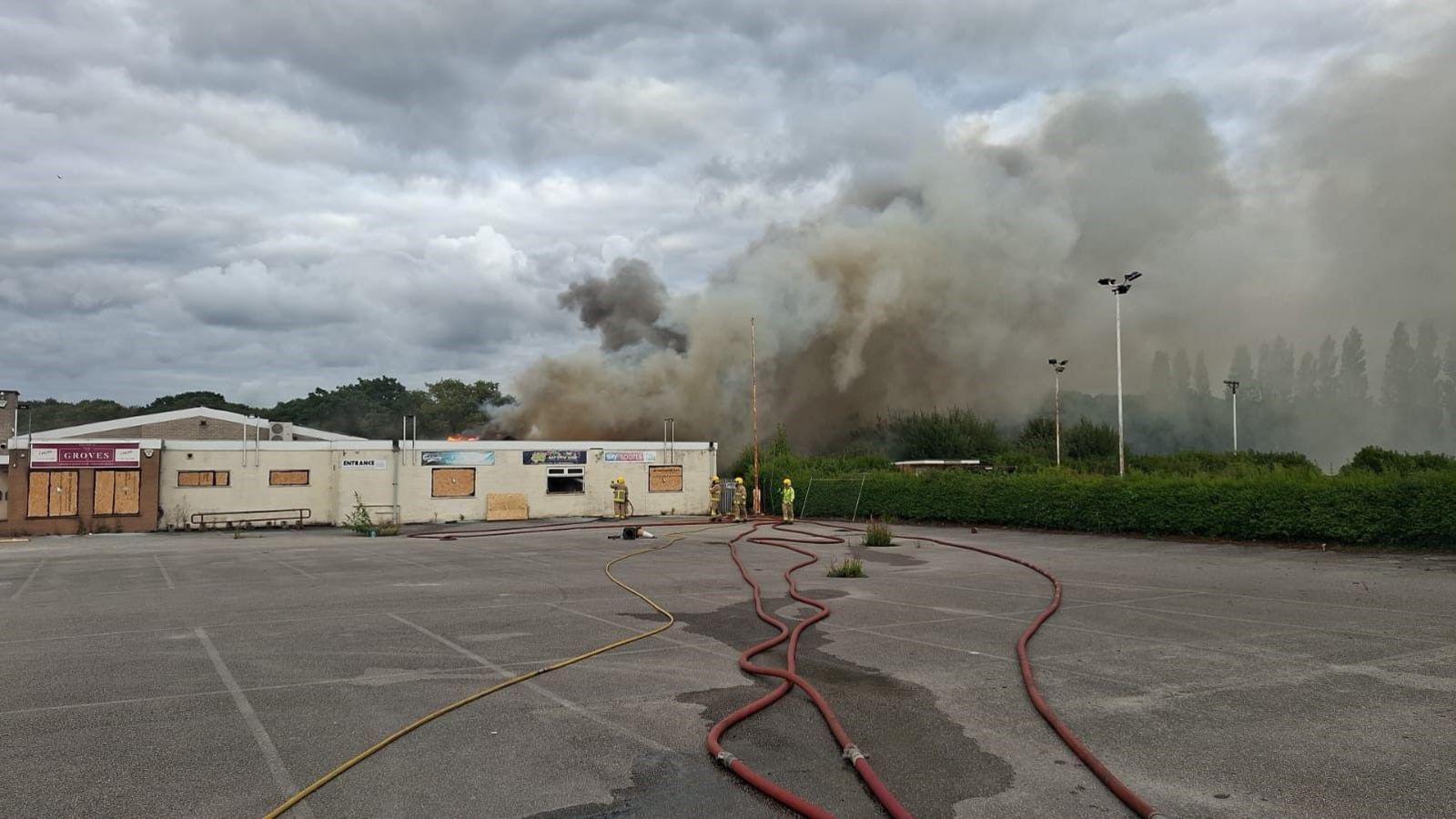 Plume of smoke drifts over the building with hoses lying across the empty car park. 