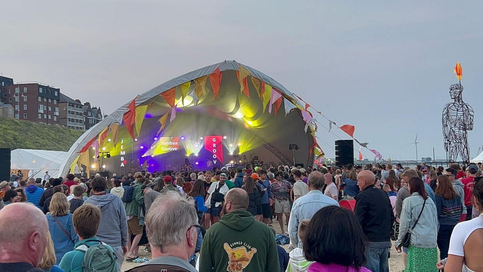 Crowds of people watch a band perform on a large stage on Lowestoft beach during First Light Festival.
