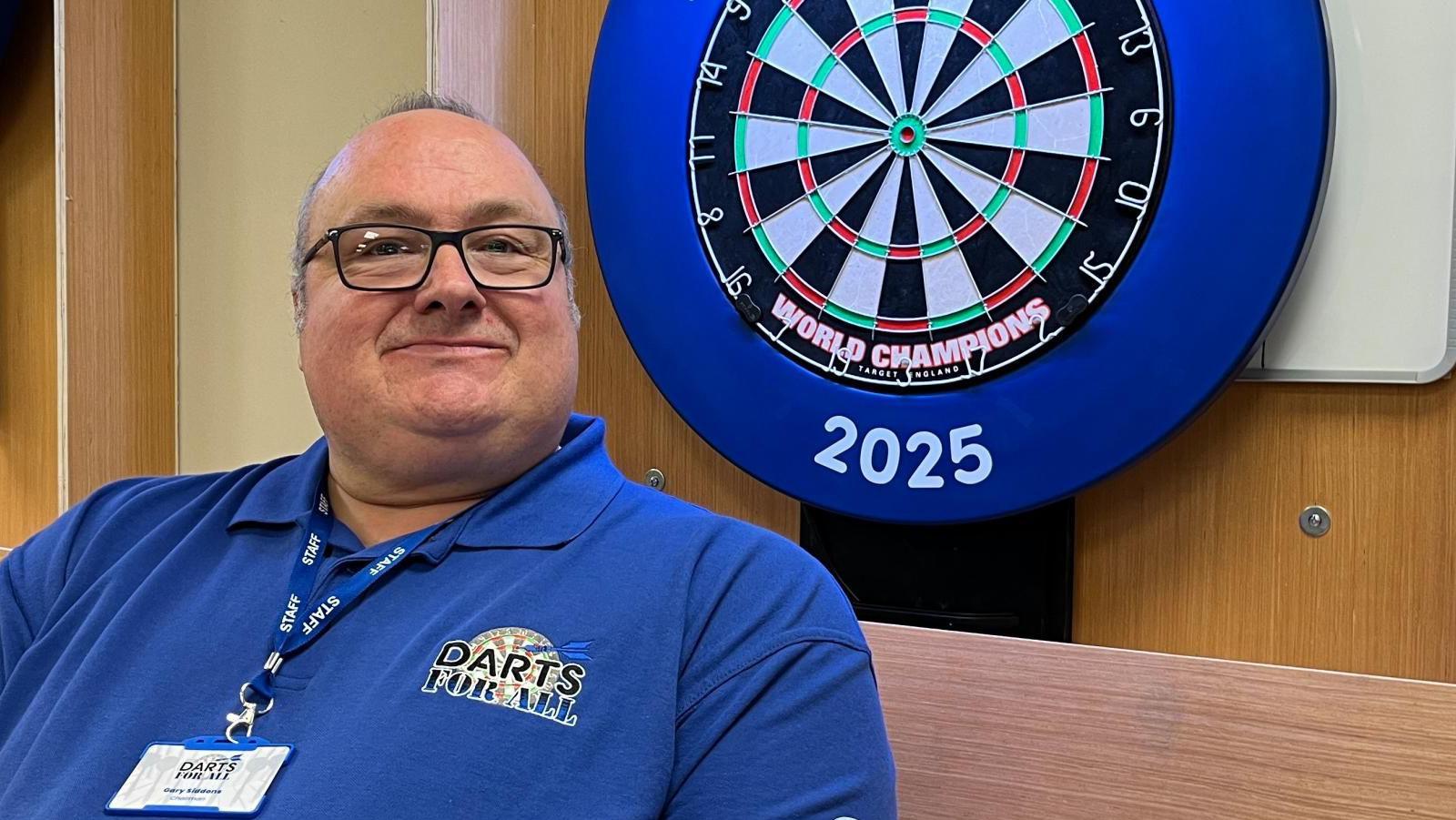 Gary Siddons, at the John Storer House, where the first session of Darts for All took place. He is next to a darts board which moves vertically.