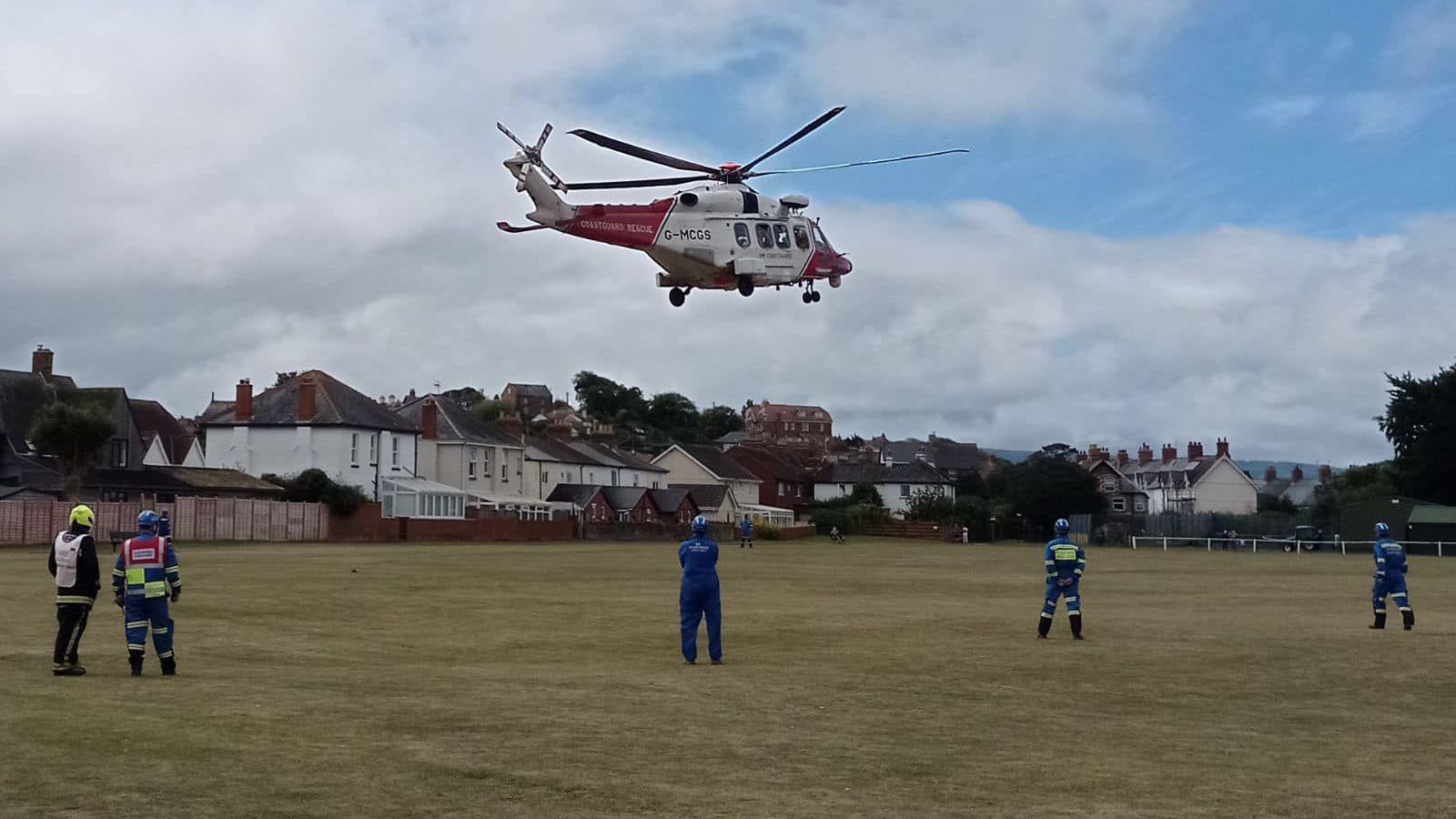 A red and white helicopter landing on a playing field with rescuers standing on the ground