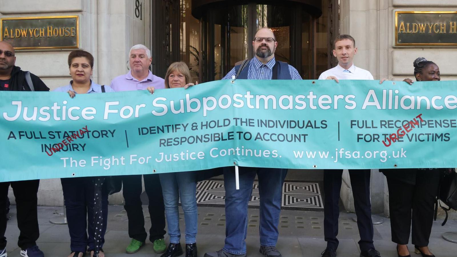 Subpostmasters stand holding a large sign calling for justice