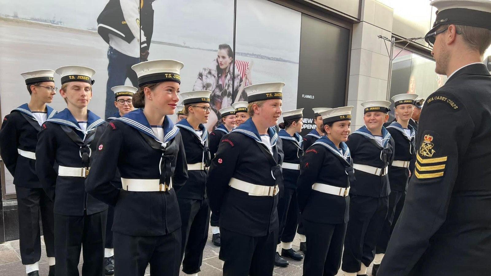 A group of young sea cadets stand at attention in uniform in front of a commanding officer