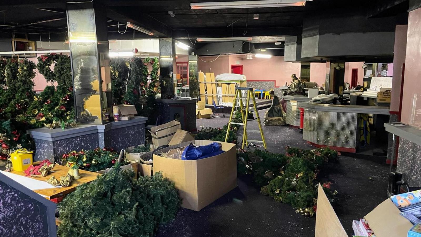 The interior of the old Troubador nightclub as it is now, with mirrored panels, old carpet and strip lights, and filled with large Christmas decorations, multiple cardboard boxes and a ladder.