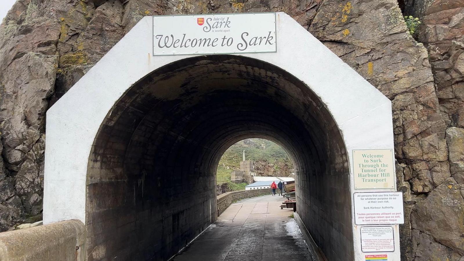 A sign that says Welcome to Sark above a tunnel