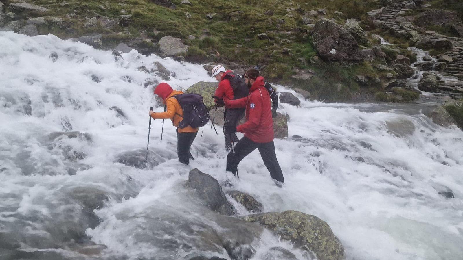 Mountain Rescue volunteers pick their way across a swollen and dangerous gully where the stream has flooded.