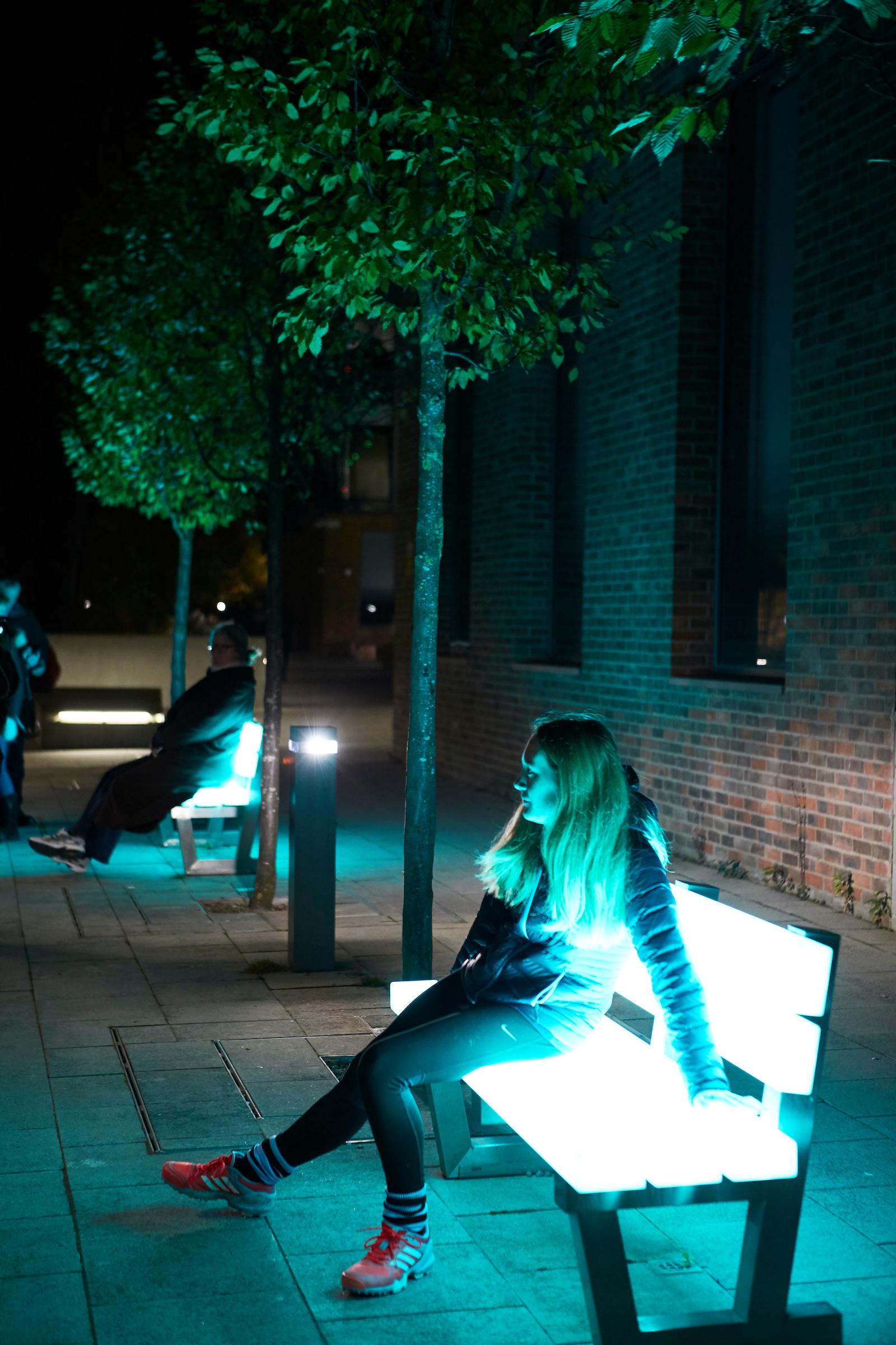 People sit on benches shining with bright blue light.