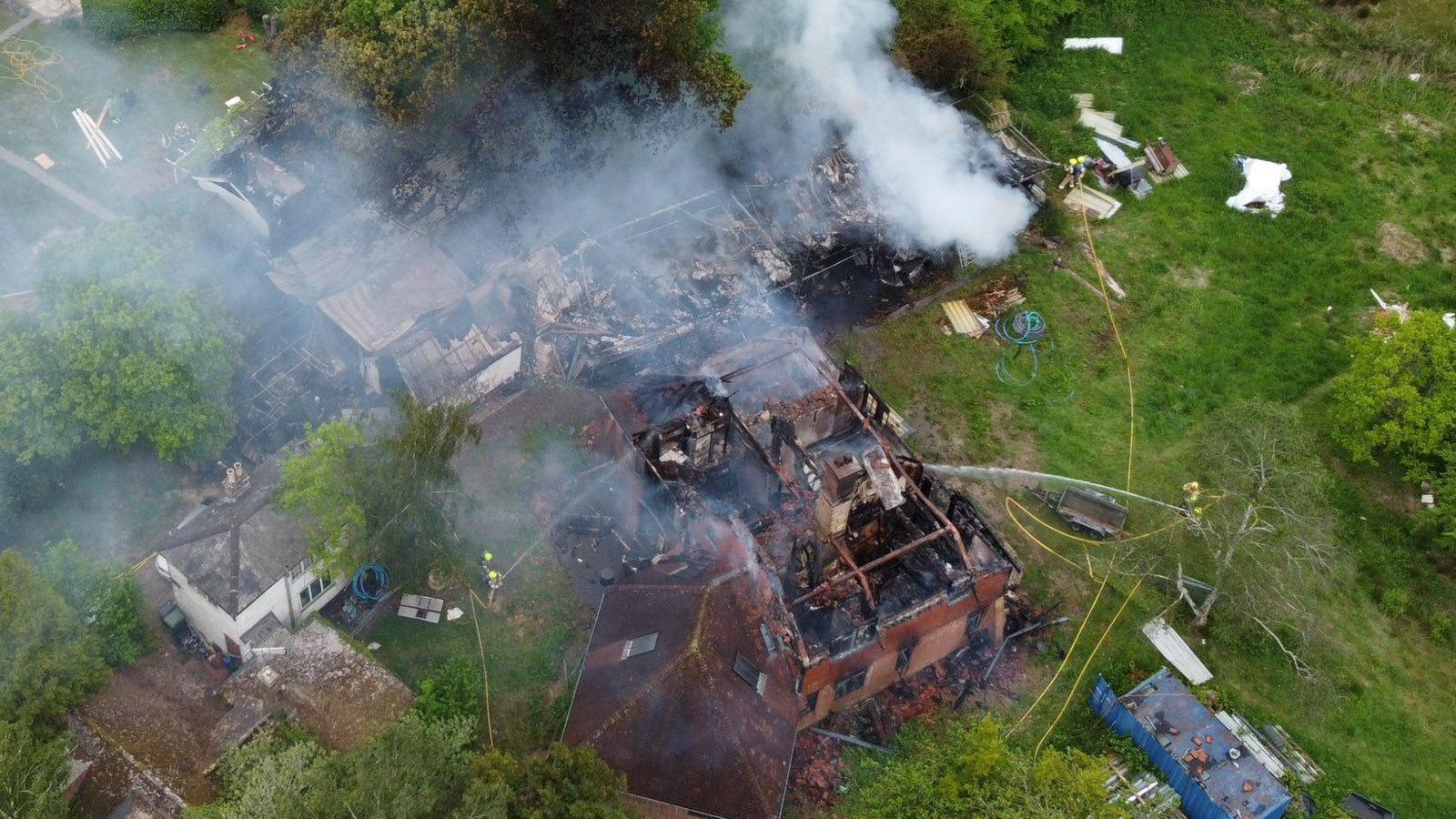 A large property smolders as firefighters spray water onto it.