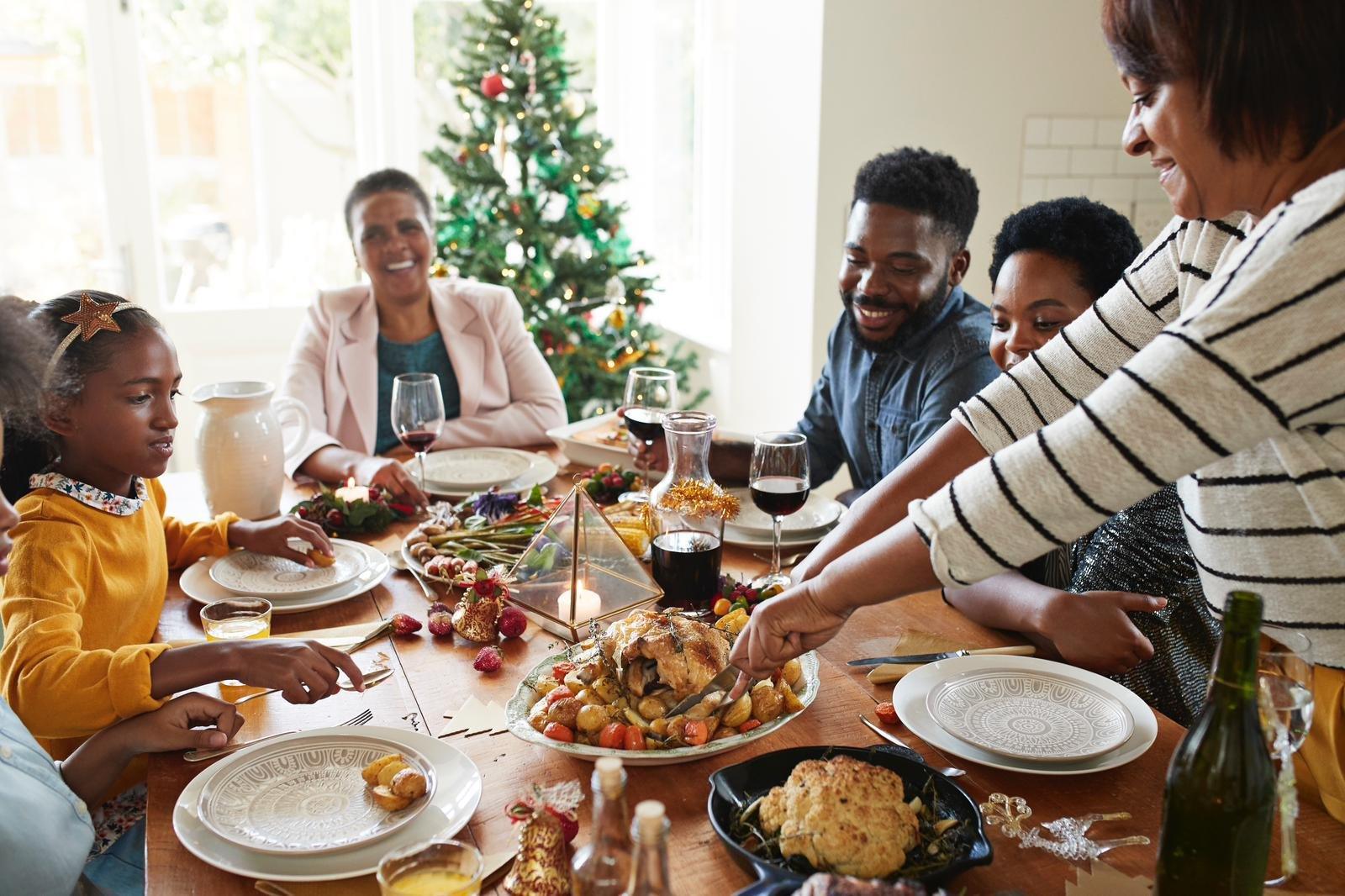 Woman cutting meat for family and friends on dining table at home during Christmas dinner