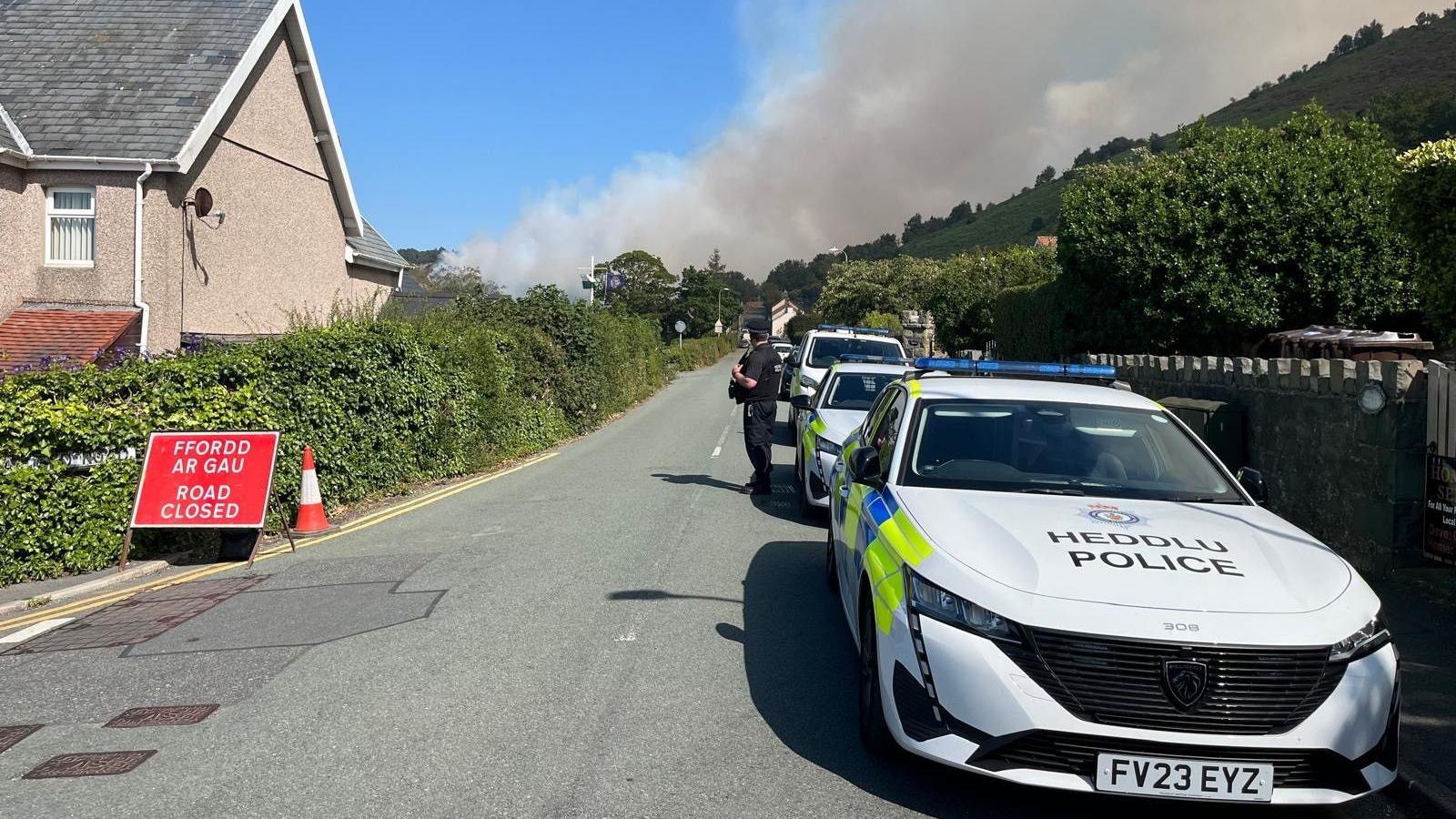 Police cars are parked connected the close a roadworthy adjacent motion tin beryllium seen connected the left. There is simply a immense unreality of fume rising into the entity implicit the hillside with houses seen connected the street.