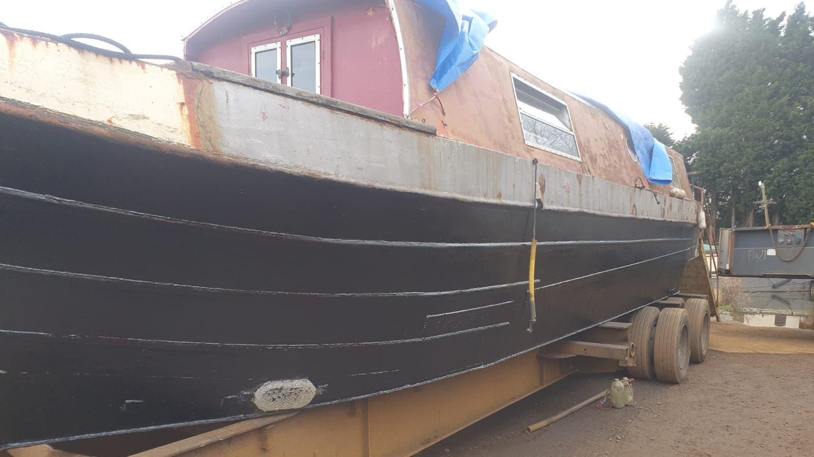 A narrowboat, sat on a heavy duty trailer, while undergoing restoration