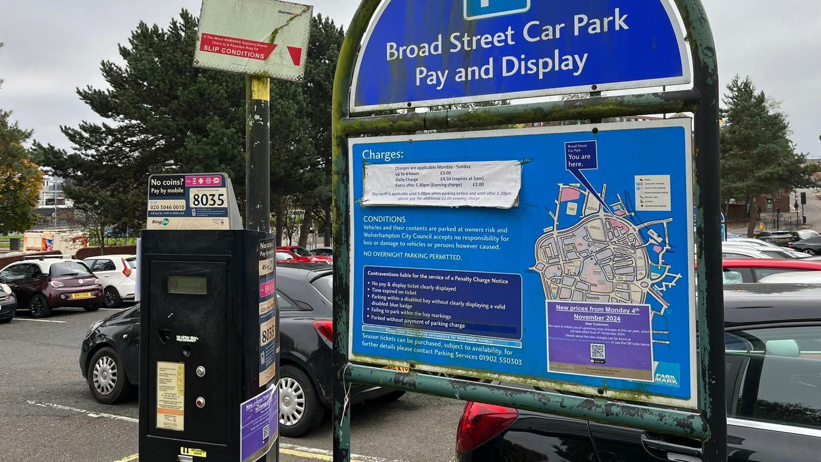 Broad Street Car Park in Wolverhampton. Cars are in the background, behind a black payment meter and blue signage showing the fees