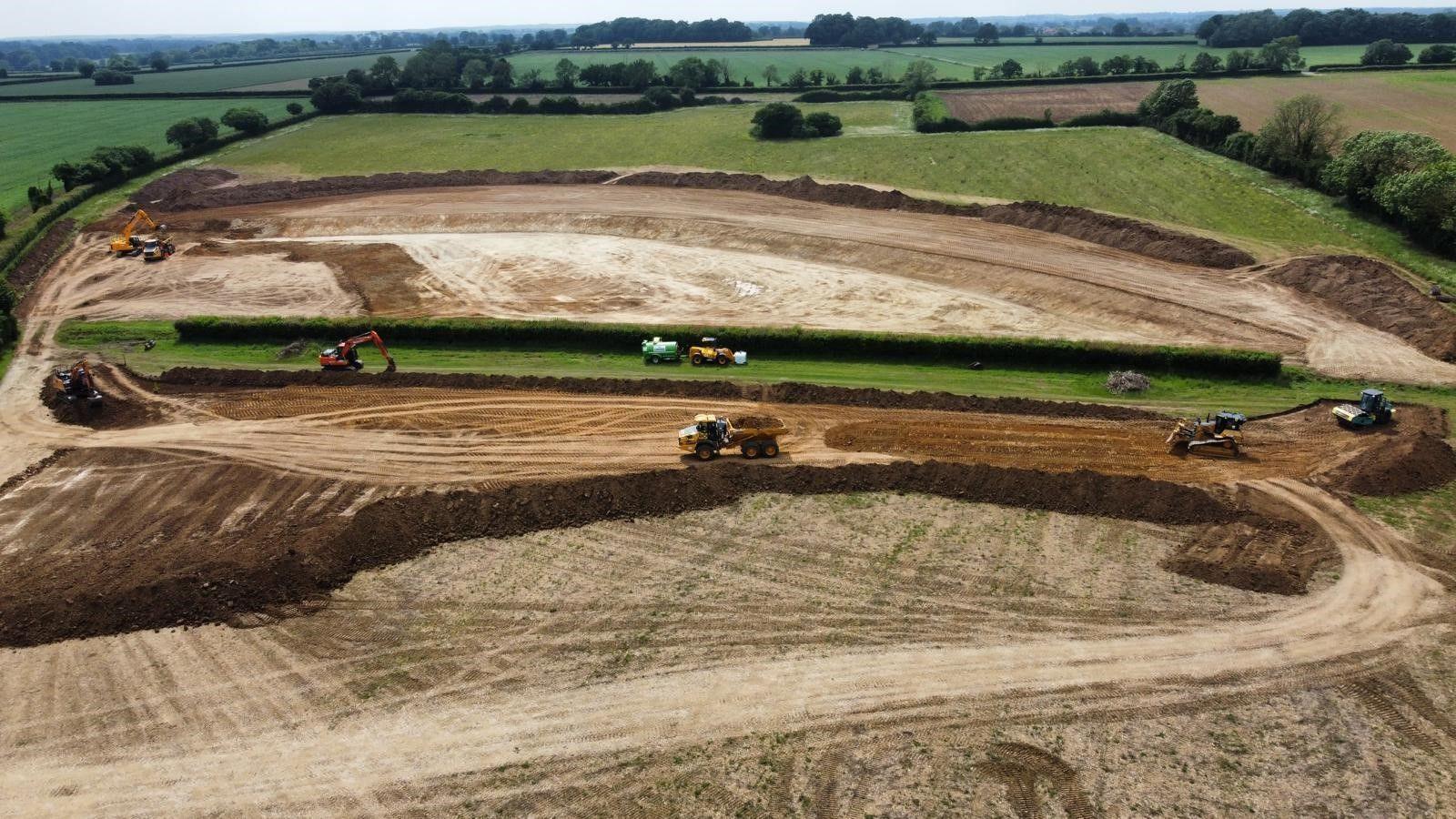 Diggers and tractors work on giant excavation of flood basins leaving tracks on soil over a vast area - see from the air