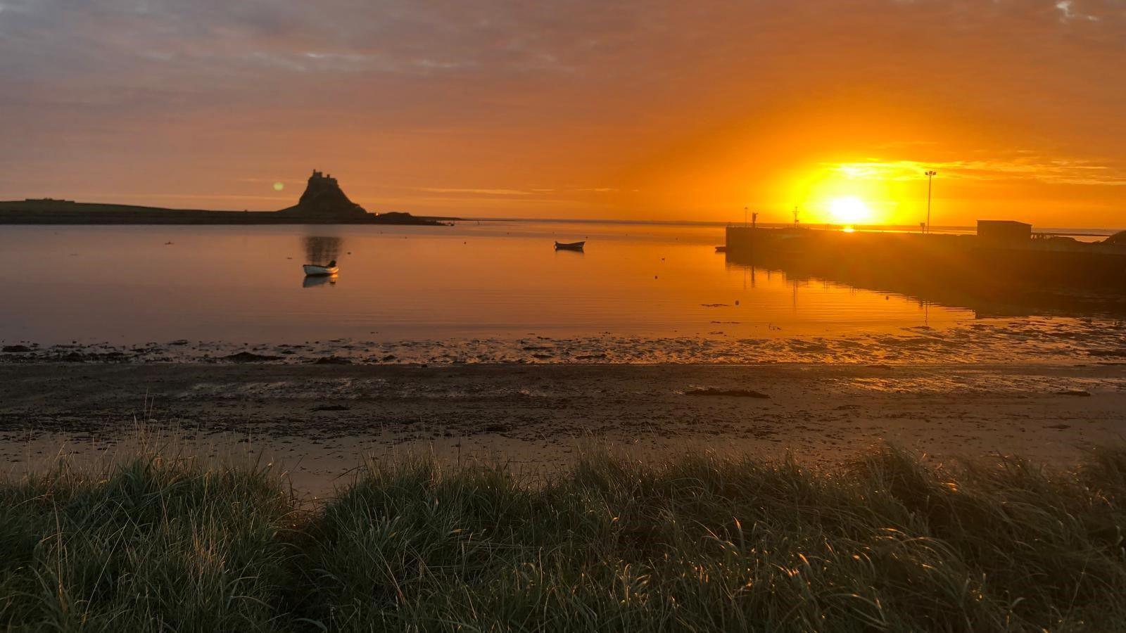 Dawn on Holy Island with the sun rising above the harbour and Lindisfarne Castle in the distance.