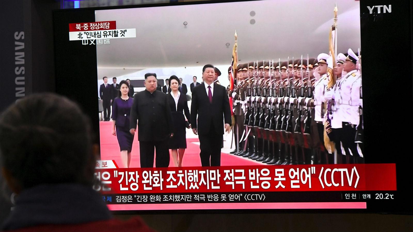 People watch a television news screen showing North Korean leader Kim Jong Un welcoming Chinese President Xi Jinping at Pyongyang airport