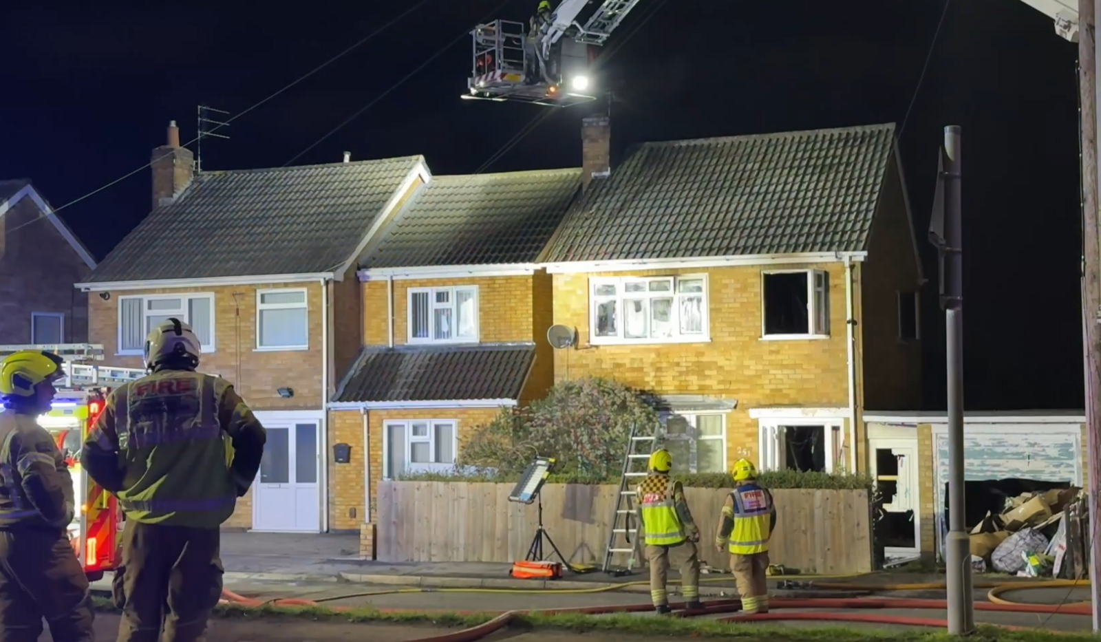 Two houses. The one on the right has windows open and four firefighters stood outside.