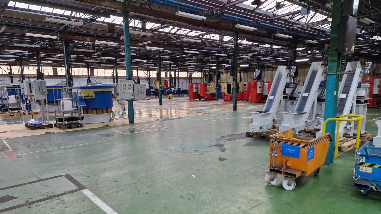 The factory floor. It is largely empty with large pieces of equipment left behind, including conveyor belts. 