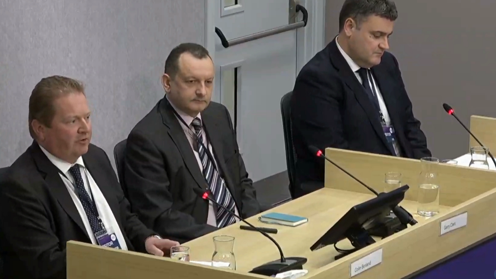 Colin Borland, Garry Clark and David Groundwater from the Federation of Small Businesses sit at a desk with three microphones and a monitor at the Scottish Covid Inquiry.