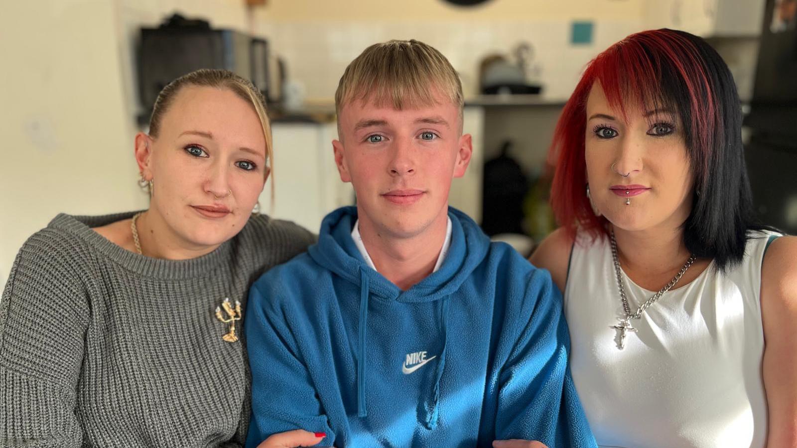 Three people sitting beside each other. A woman in a grey jumper on the left, a man in a blur hoodie in the middle and a woman in a white top with red tinted hair on the right.