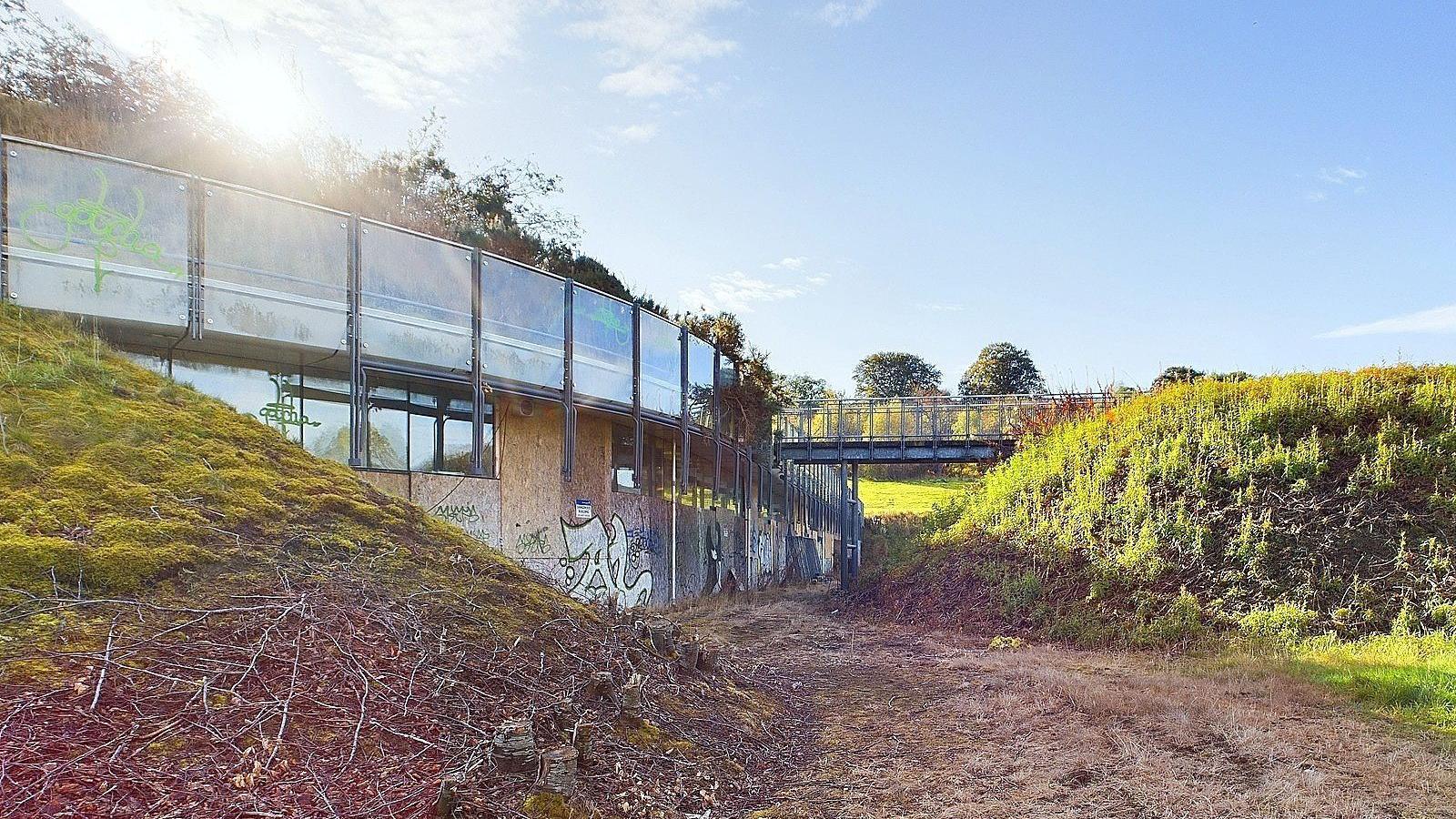 The outside of the Archaeolink Prehistory Park. The building is a mix of grass, glass and bricks. The walls are covered in graffiti 