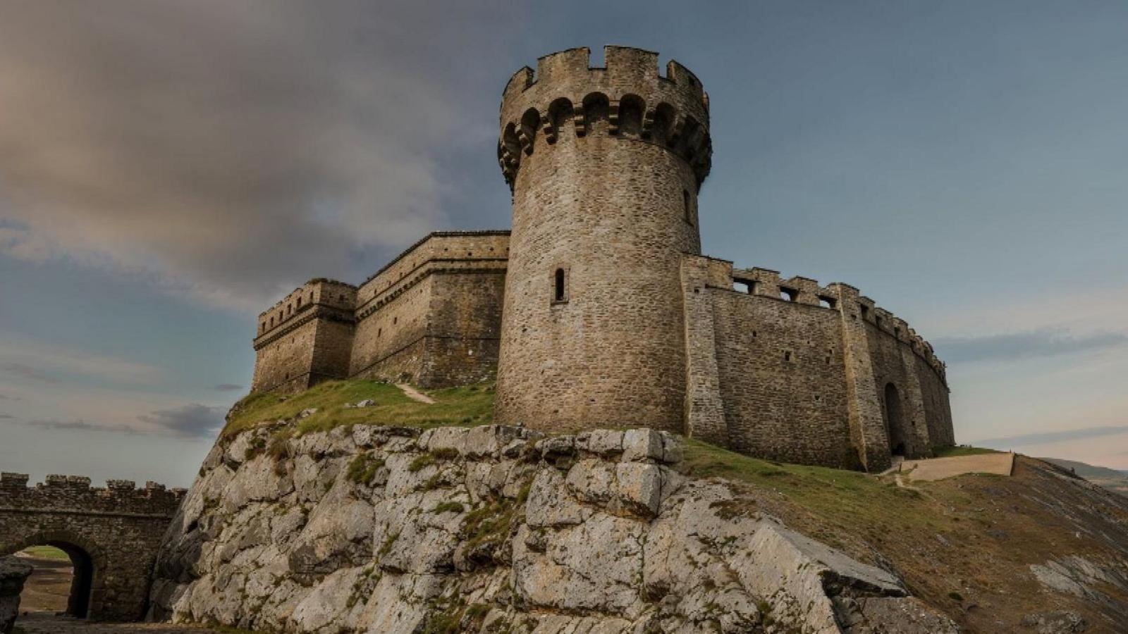 A large stone fortress with a tower sits on a rocky outcrop. 