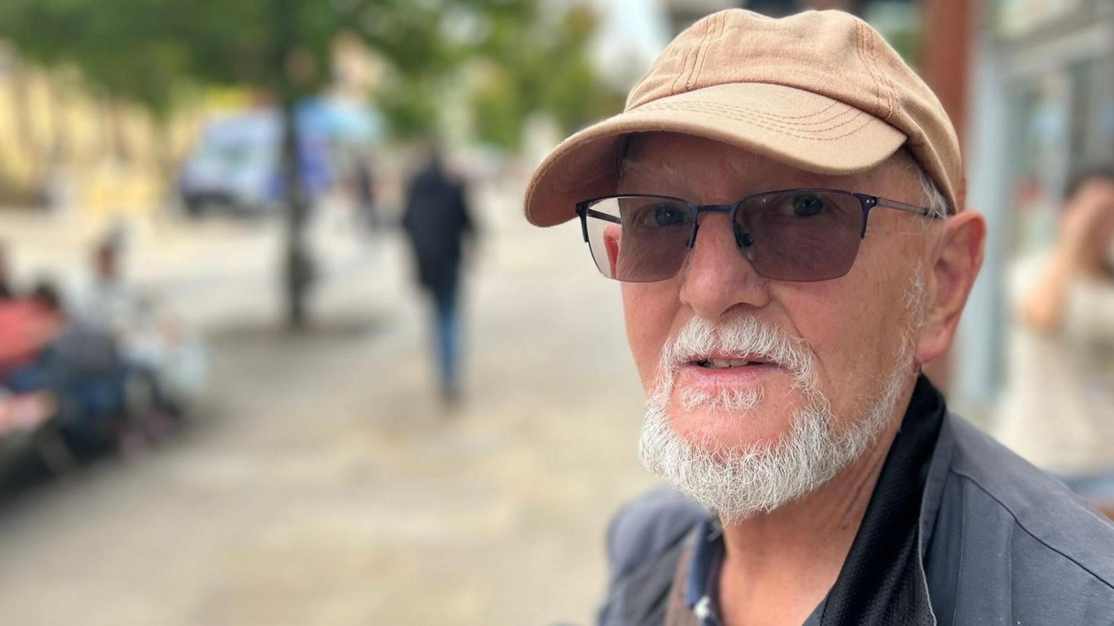 Keith Andrews, with a white beard, wears sunglasses, a beige cap and a navy jacket.