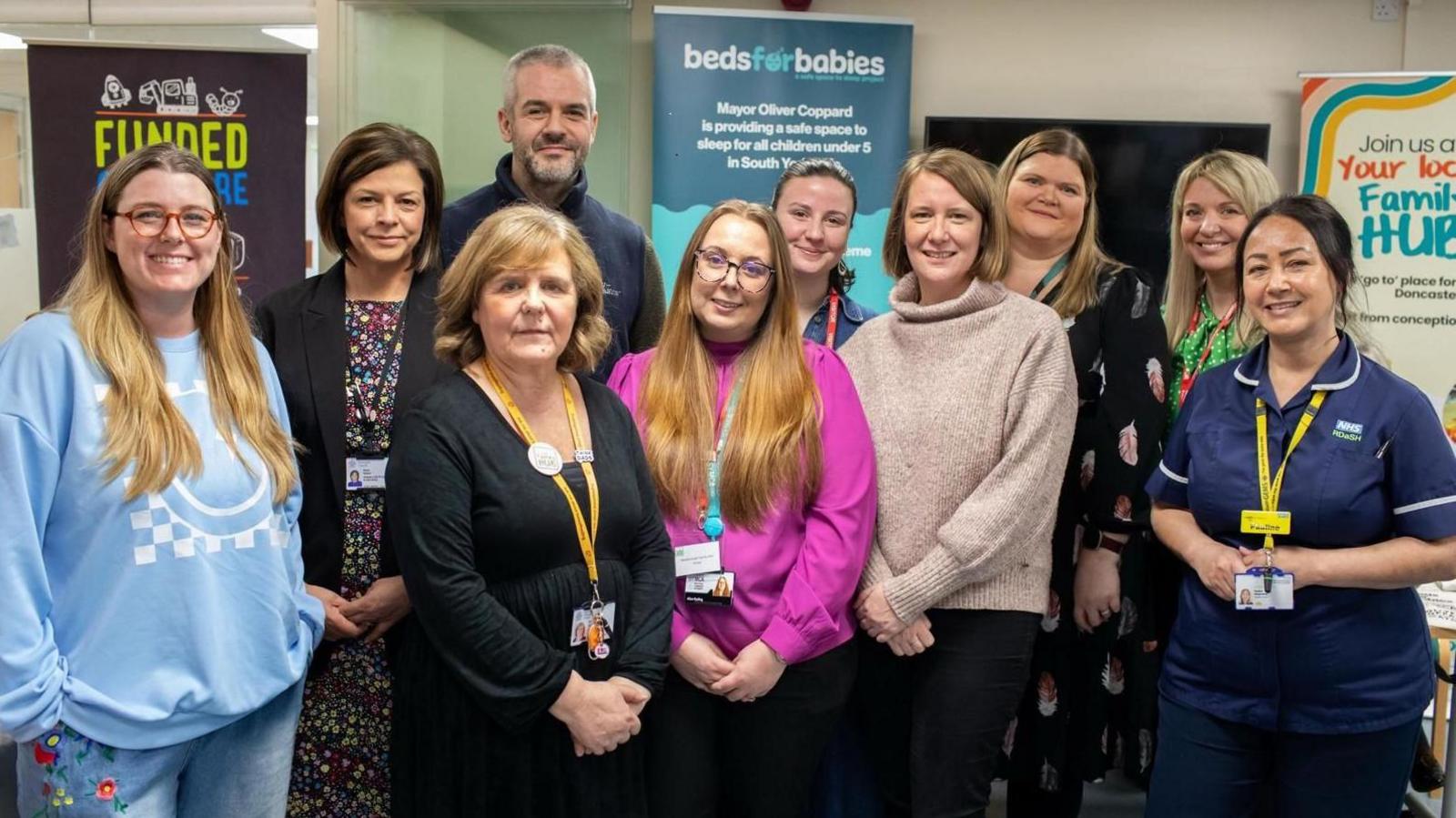 A large group of adults smiling huddled together in a busy looking community centre