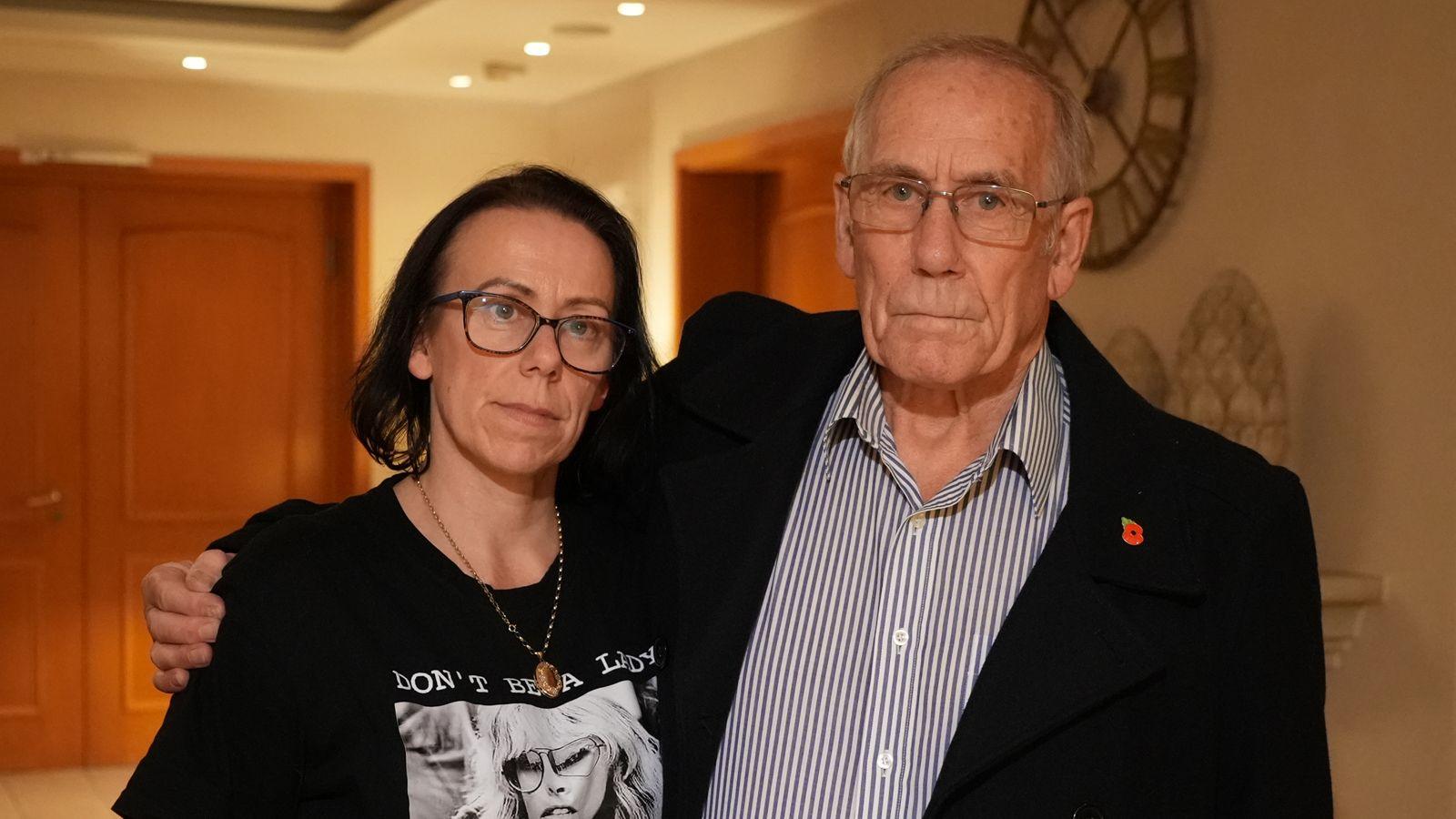 Natasha has shoulder length dark hair and is wearing glasses, a black t-shirt with a black and white image of a woman, glasses and a necklace with oval pendant. Her father Richard stands on her left with his arm around his daughter's shoulders. He is wearing a black jacket over a white and black striped buttoned shirt and glasses. They are standing in a corridor with wooden doors behind them.