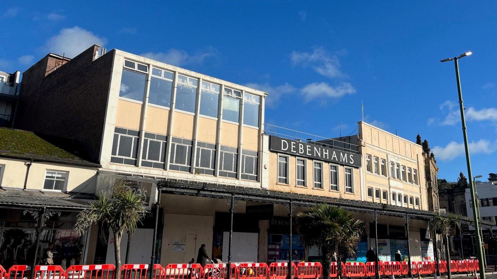 The former Debenhams site overlooking the harbour in Torquay with red and white barriers in front of the building