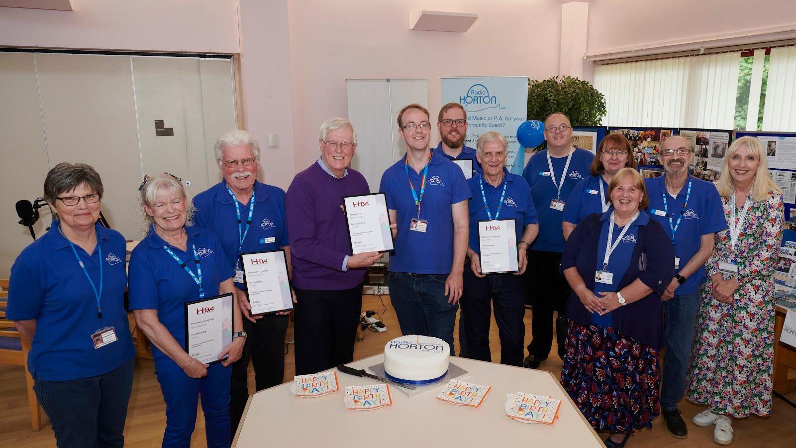 A row of people, radio volunteers, all holding certificates with John Craven in the middle