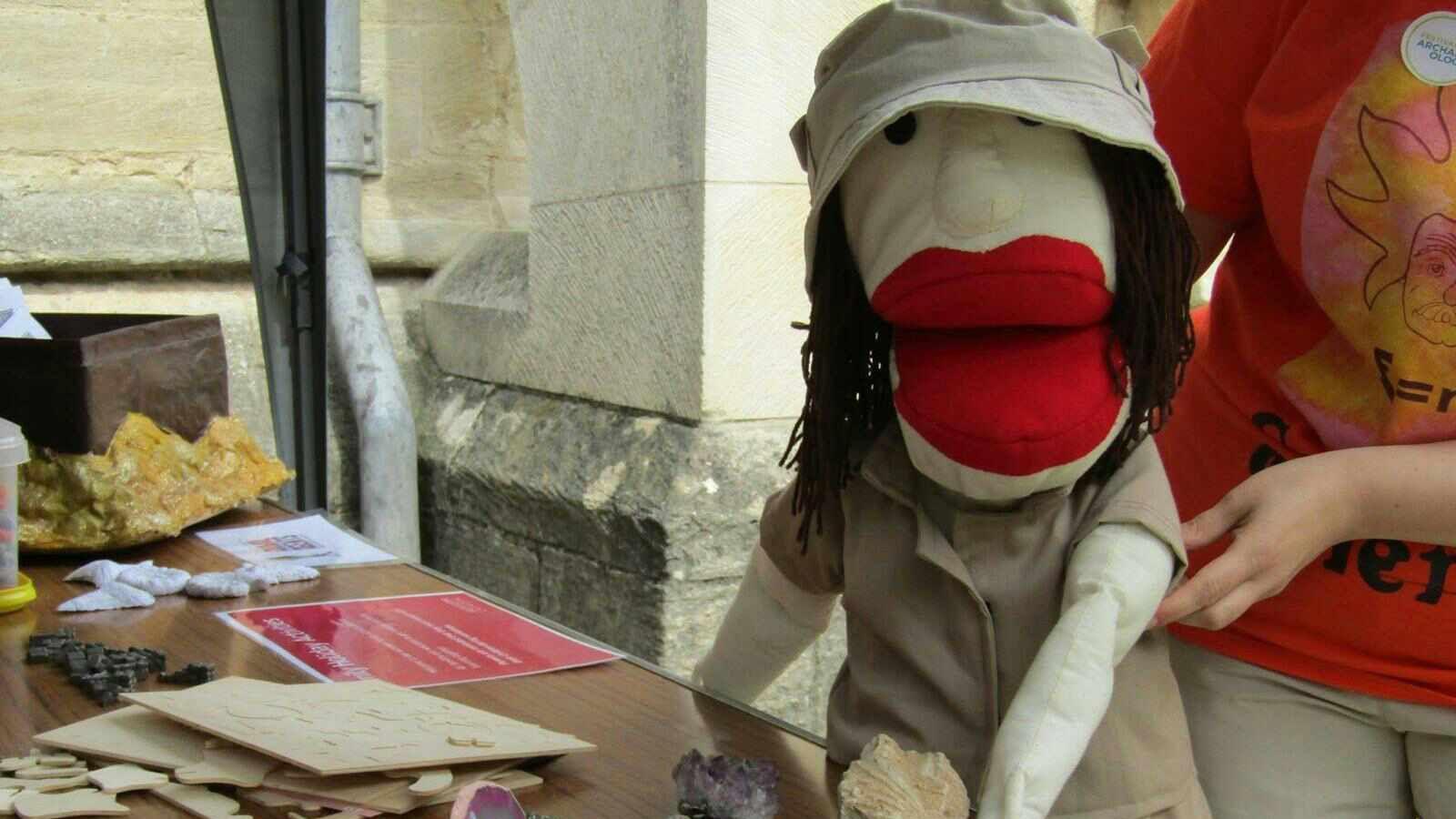 A puppet of Mary Leakey, which has big red lips and is wearing grey overalls