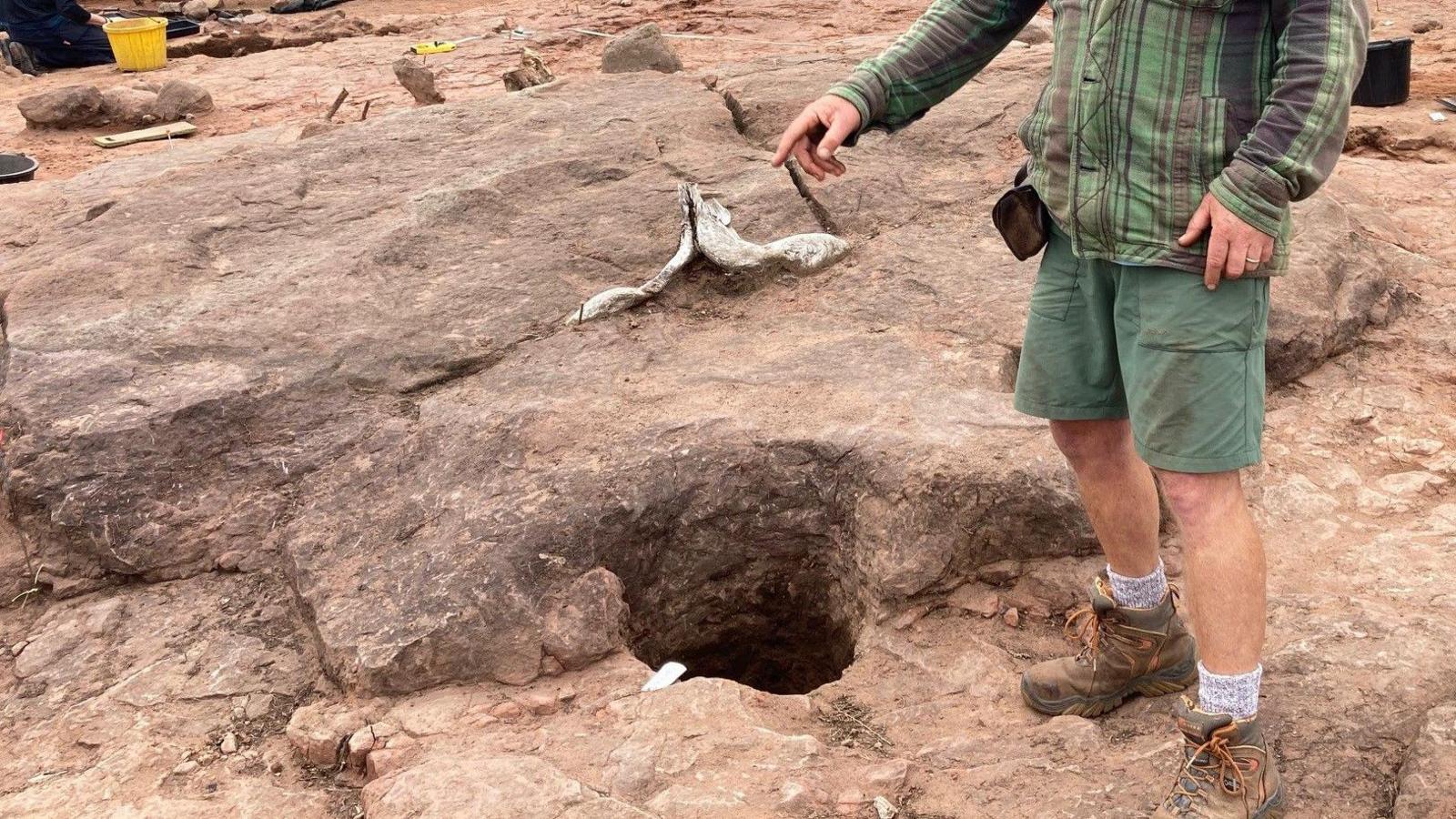 A man in green shorts pointing at a hole in the rock