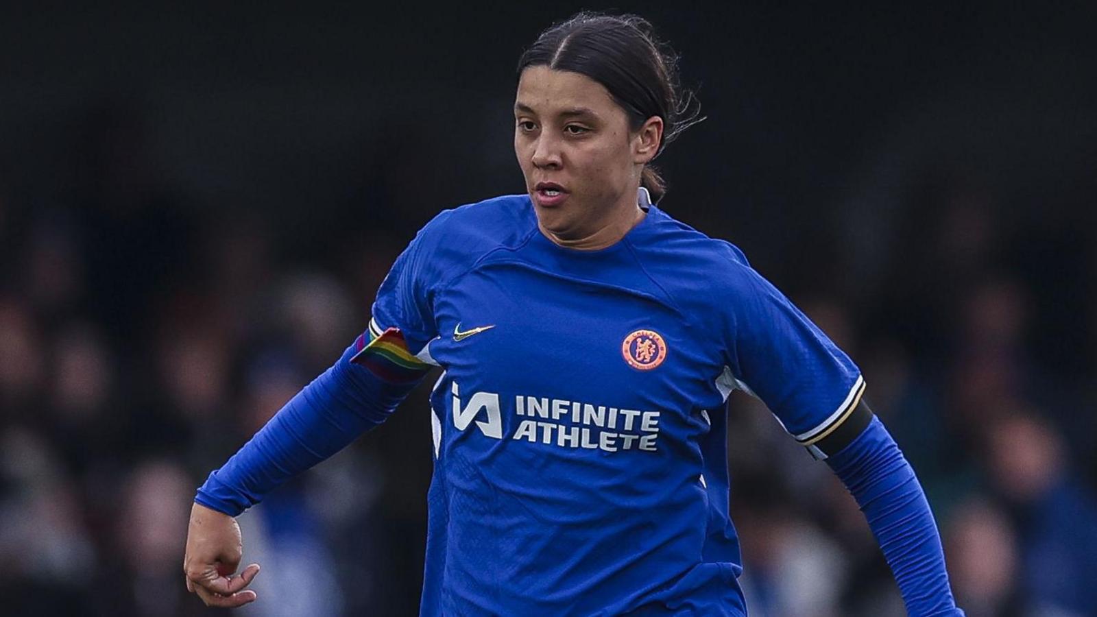 Sam Kerr on the pitch playing football. She wears a blue Chelses football strip and her dark hair is tied back as she runs forwards