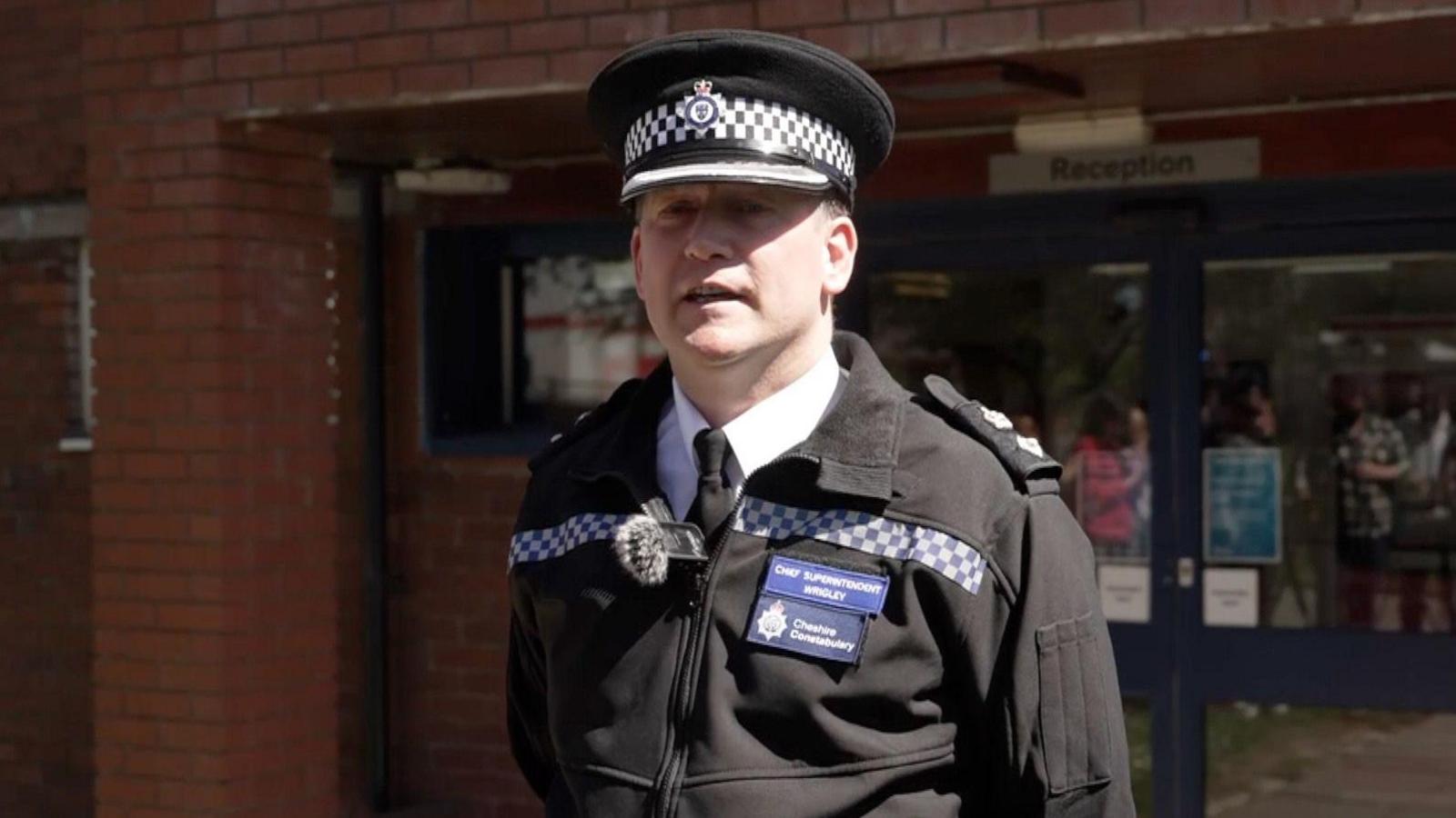 A police chief superintendent, wearing a black police uniform. He is standing outside a police station and is looking side-on from the camera.
