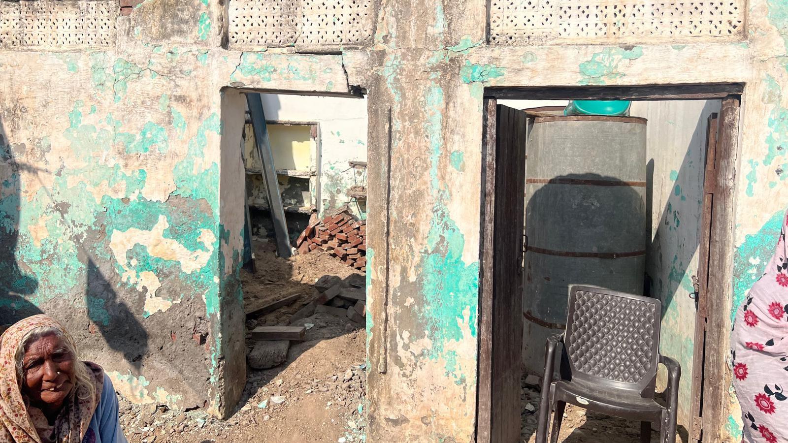 A dilapidated building with peeling paint, no floor, and piles of bricks.