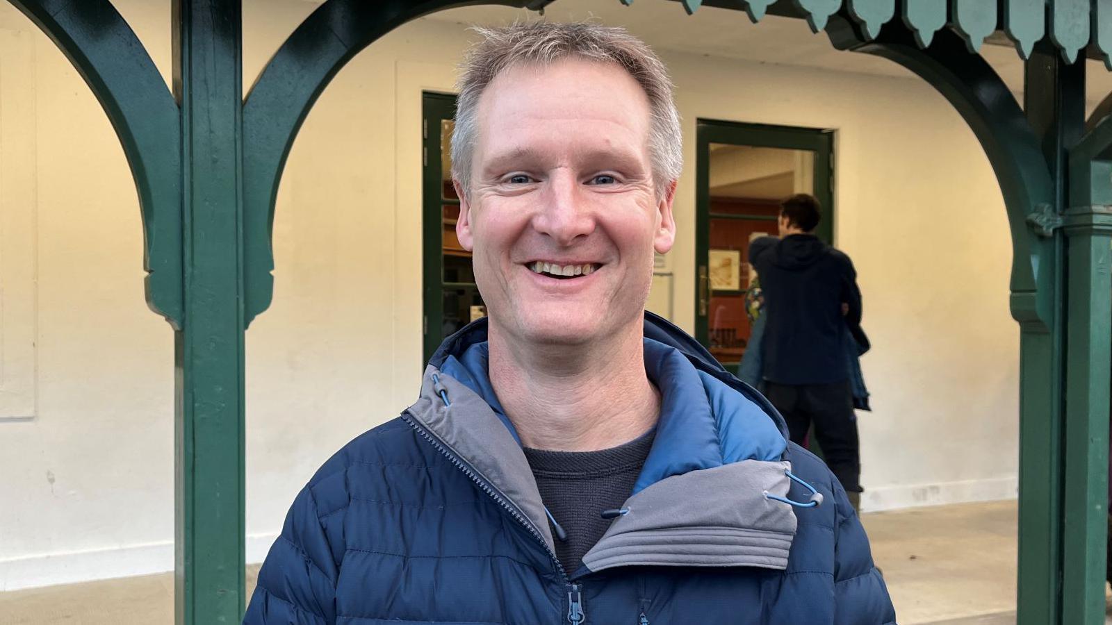 Dan, who is smiling, is wearing a blue jacket and is standing outside the front of Strathpeffer Pavilion.