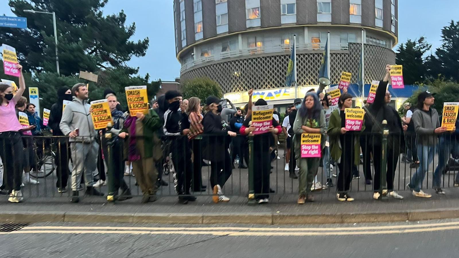 A group of people gathered outside a circular building holding up anti-racism placards