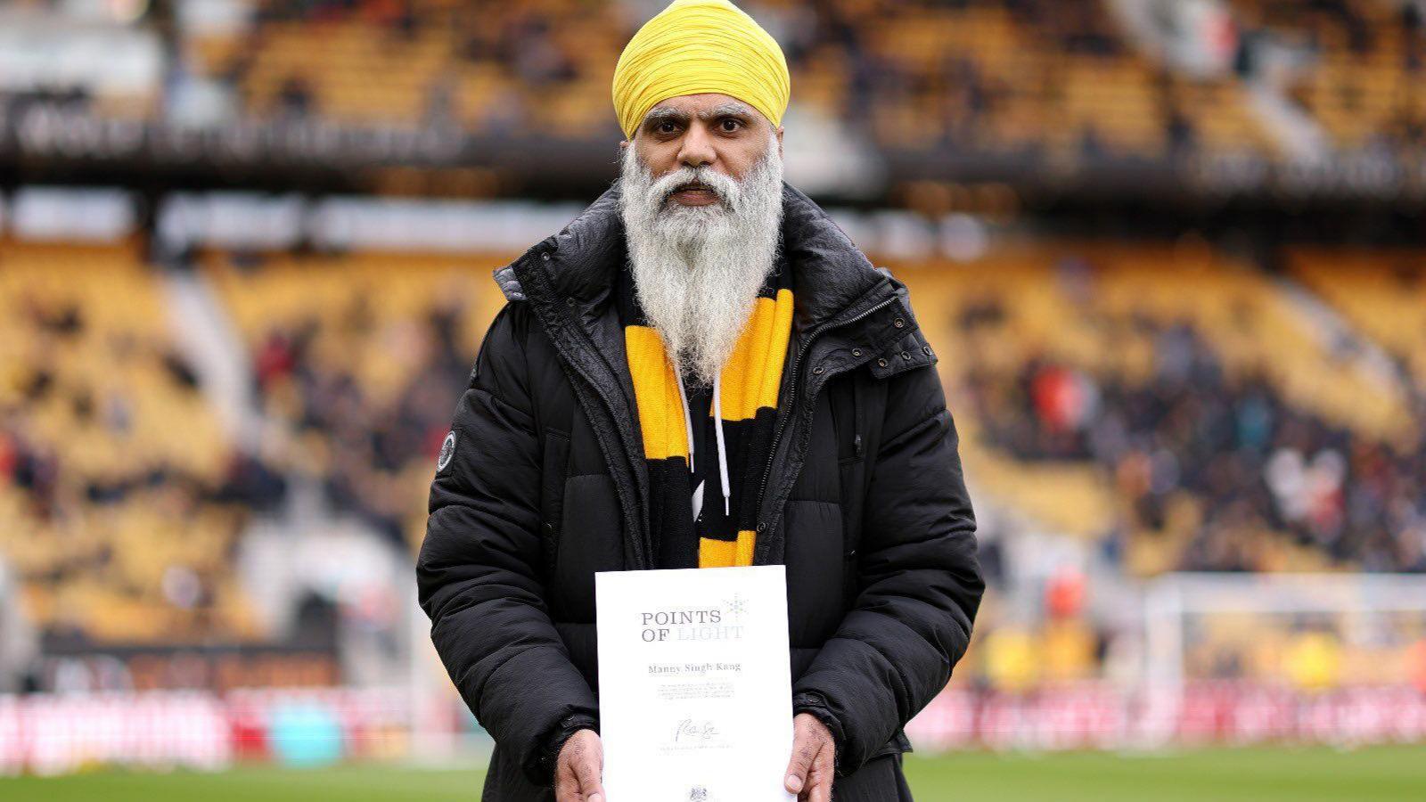 Manny Singh Kang holding a certificate at Molineux Stadium