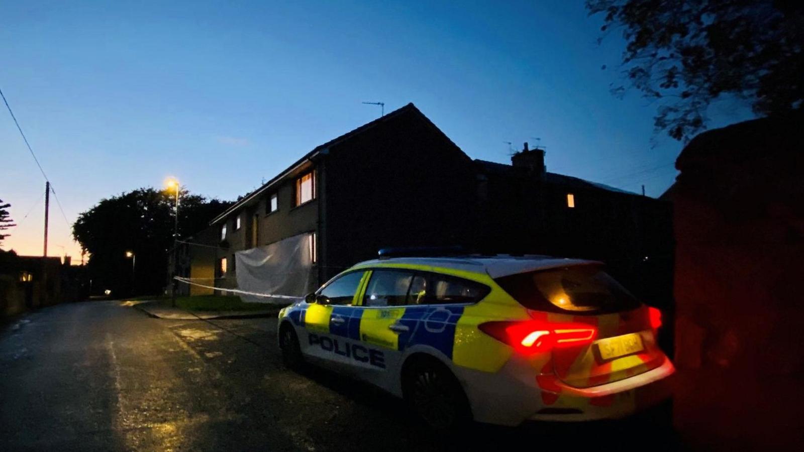 A police car outside a house, which taped off, at dusk