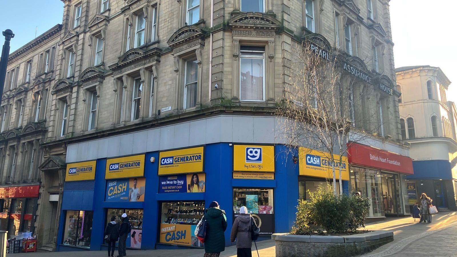 Blue and yellow signs adorn the front of multi-story building. Above the ground floor it is made of stone and had decorative features around the tall windows on each floor.