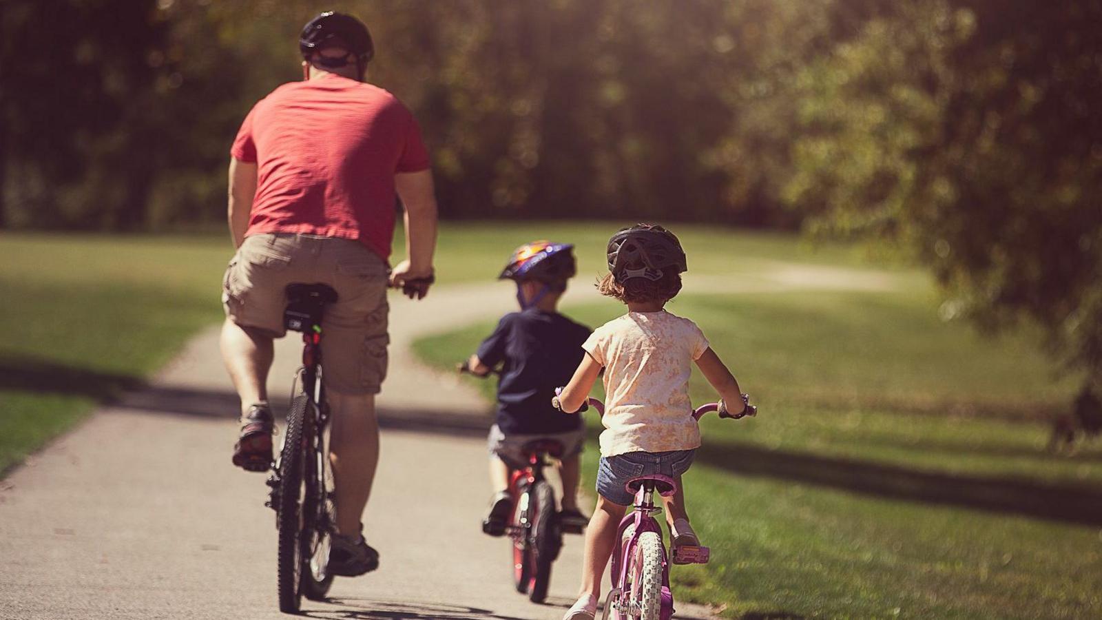 A father with two children cycling on a path in a forest