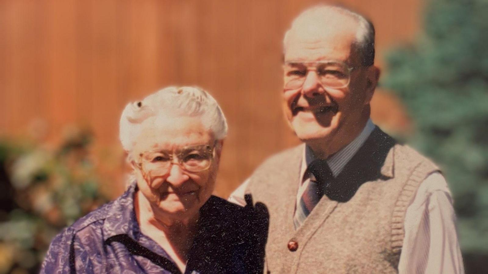 An old photograph of the late Dr Wally Baldwin and his wife, Wilma. They are smiling and there are trees in the background. 