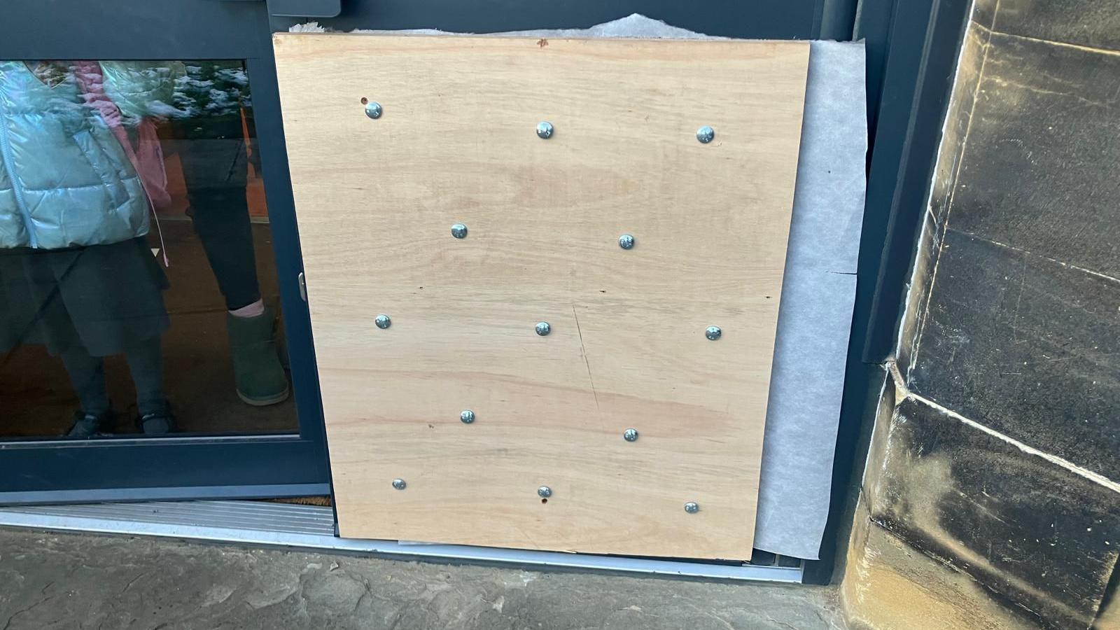 A photograph of a plank of wood installed to cover the smashed glass of doors at a nursery school in Hipperholme.