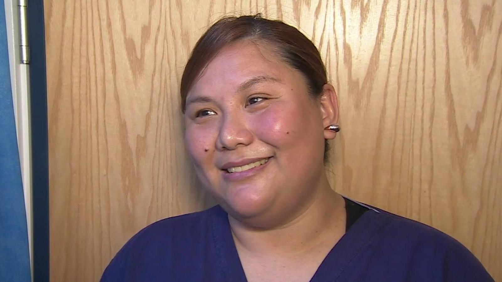 Healthcare assistant Fran Argente wearing dark blue scrubs. She has her hair tied back and is standing in front of a wooden door