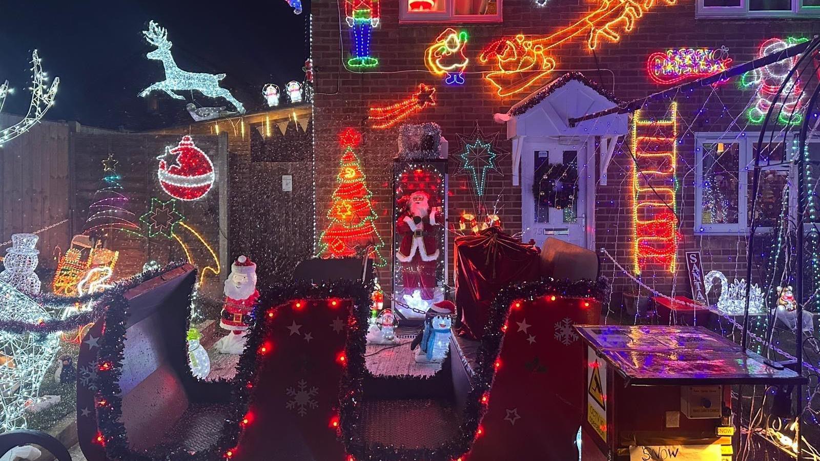 The house is covered with numerous lights and decorations with others in the front of the garden