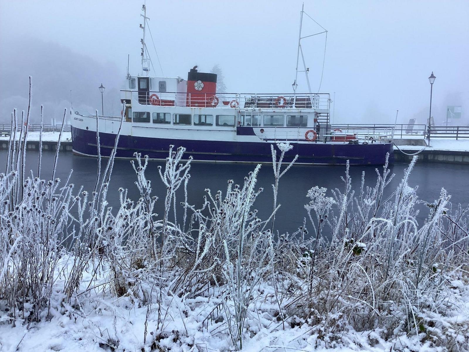 A boat moored in a lake with fog behind a bank covered of tall grasses in snow and frost