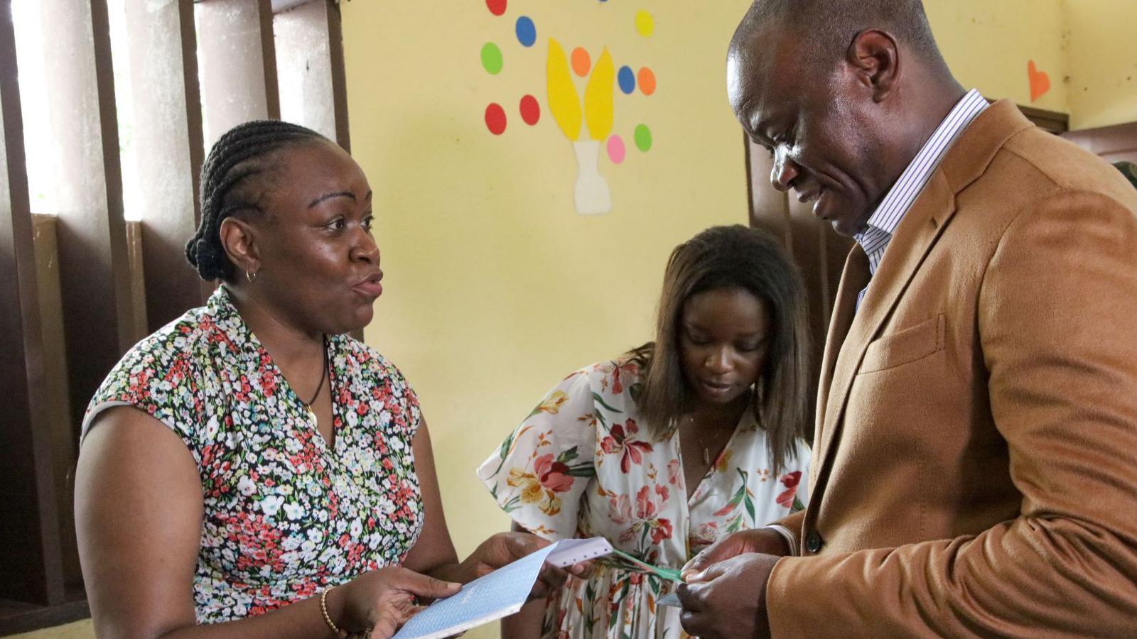 A woman in a sleeveless multicoloured dress (left) talks to transitional President of Gabon General Brice Oligui Nguema in a brown jacket (left) in a room 