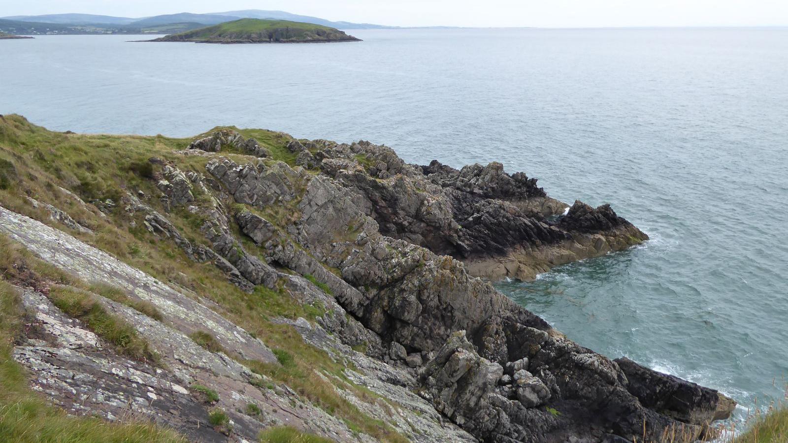 A rugged part of the Dumfries and Galloway coastline with cliffs descending towards the sea and a small island in the distance